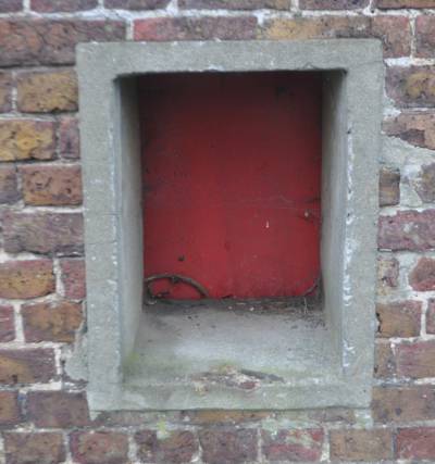 A square red door recessed in a thick brick wall