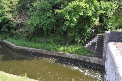 Beside the canal. two sets of steps lead to an overgrown flat area beside a lock